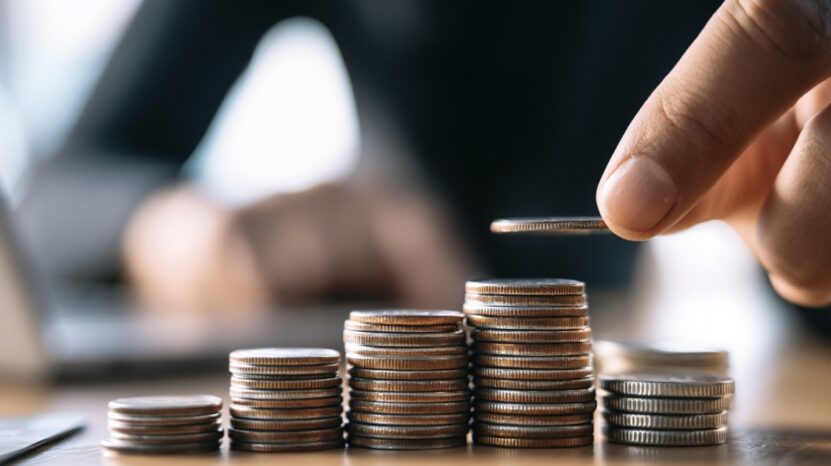 Hand placing a coin on stacked coins, symbolizing career investment and financial growth.