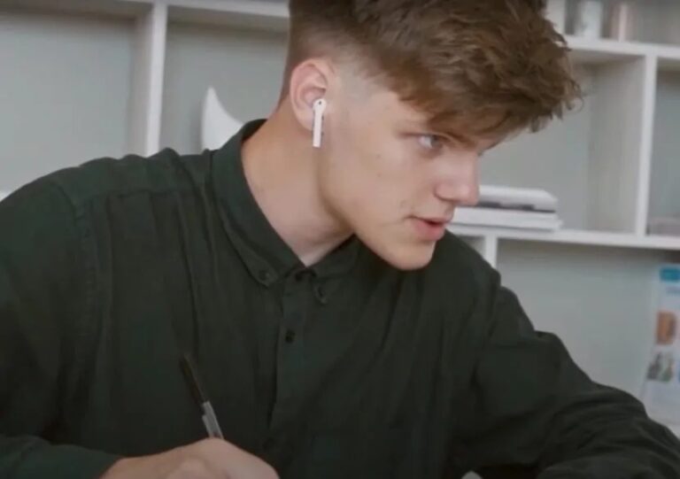 Student wearing earbuds, concentrating while writing at a desk