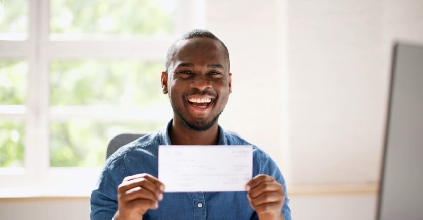 A man holds up a check, radiating joy and accomplishment