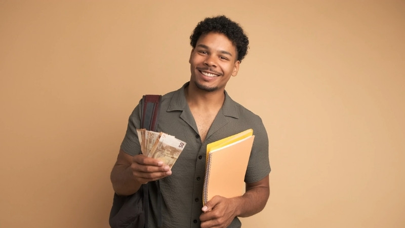 Smiling student holding notebooks and a fan of cash