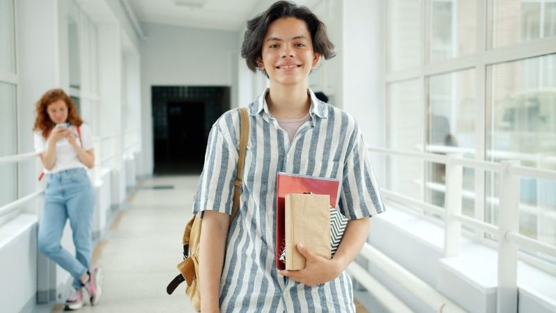 Smiling student holding books and a lunch bag
