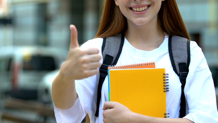 A student gives a thumbs-up, smiling while holding notebooks