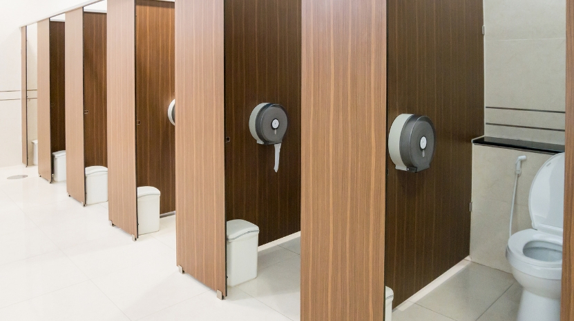 School restroom with stalls, toilet paper, and waste bins