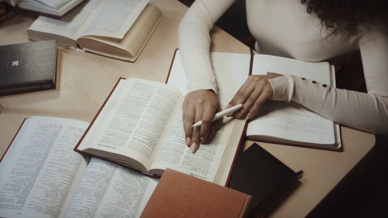 A person studies alone with open books and notebooks on a desk, writing notes without a clear study plan