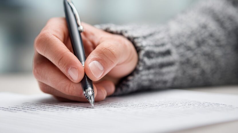 Close-up of a hand holding a pen while editing a printed document, symbolizing personal statement revisions