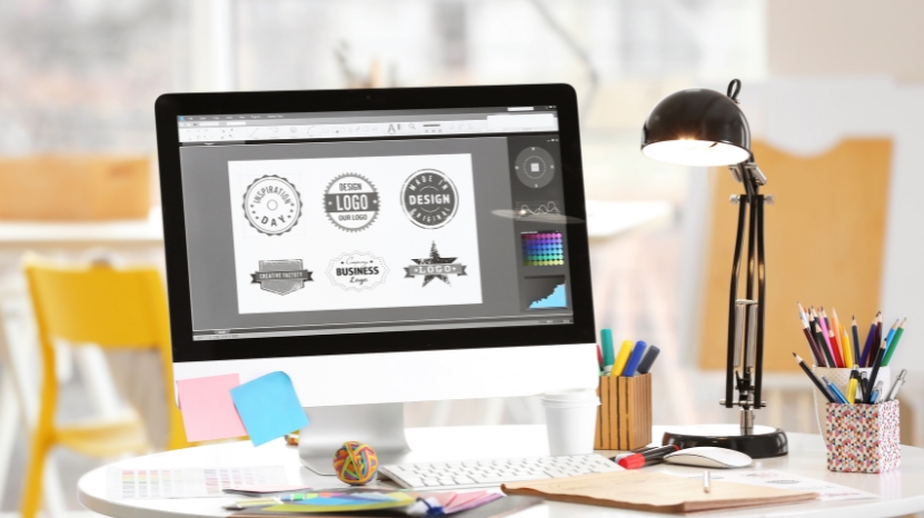 A computer screen shows a graphic designer creating logo designs
