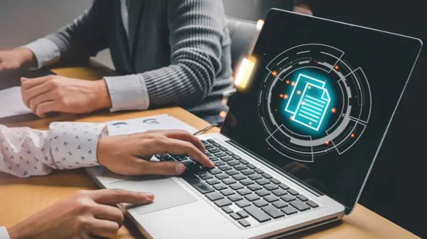 Two people work on a laptop with a digital security icon, focusing on protecting a learning management system