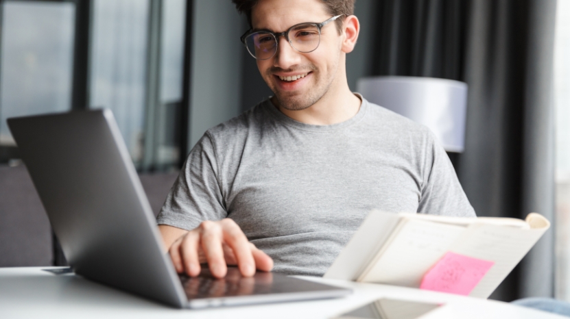 A man sits at a desk with a laptop and notebook, exploring hosting and licensing options for a learning management system
