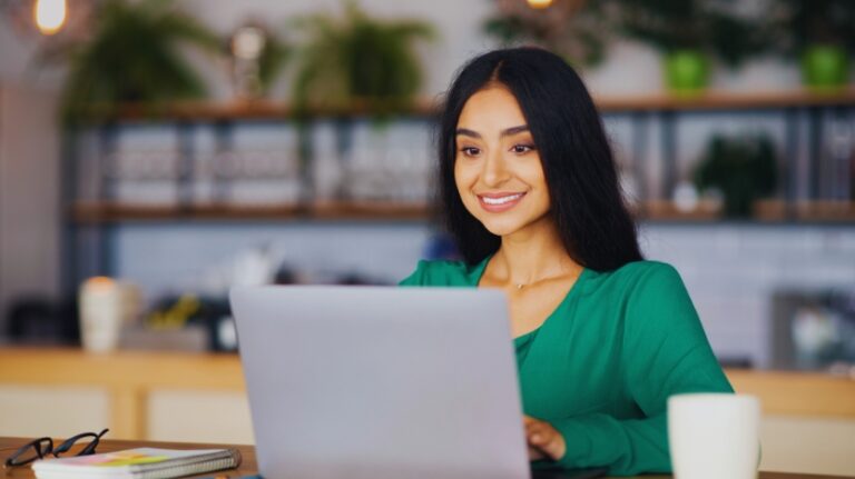 A young woman sits at a laptop in a bright cafe, building work experience before college graduation