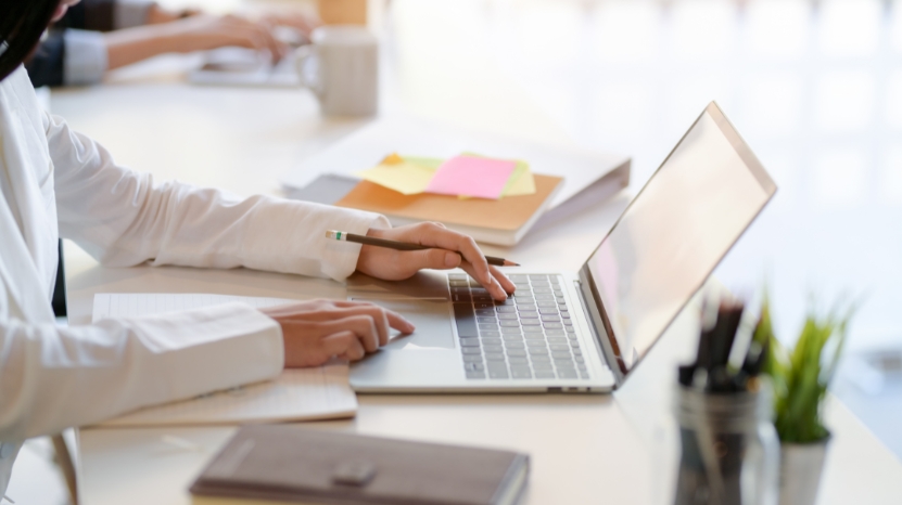 A teacher works on a laptop at a bright desk, managing courses through a learning management system