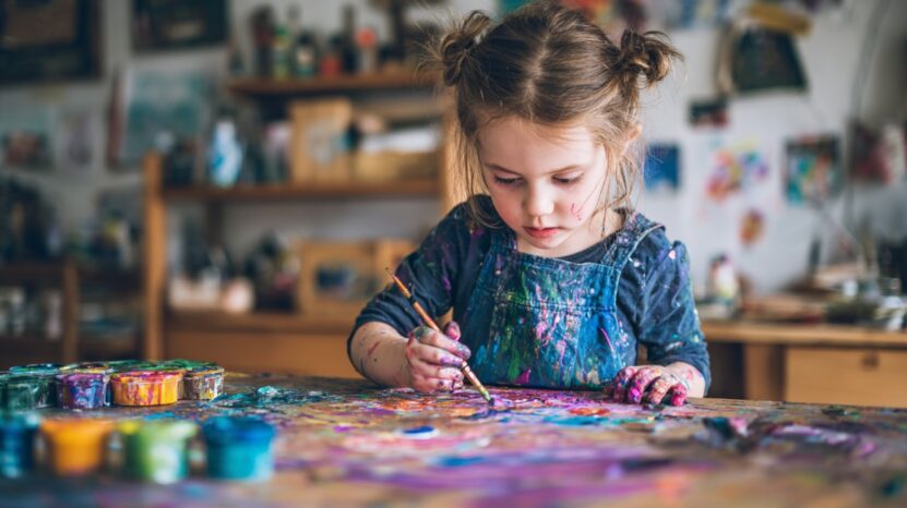 Young girl painting with bright colors at a messy, colorful art table