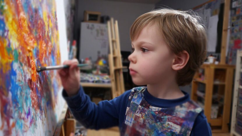 Child intently painting on a colorful canvas in an art studio