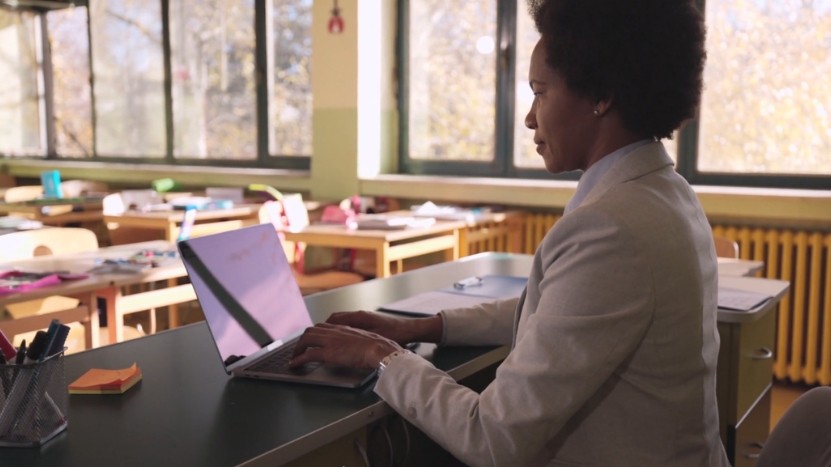 A teacher works on a laptop in a classroom, showing how automation supports teacher productivity