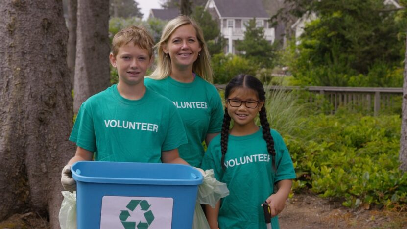 Group of children and an adult volunteering outdoors, holding a recycling bin