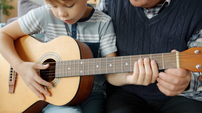 A child learning to play the guitar with guidance from an adult