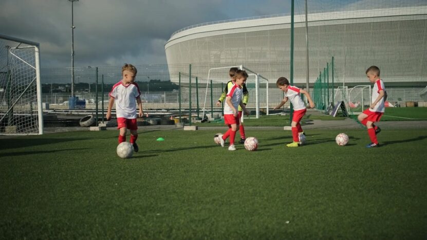 Young children practicing soccer drills on a field in sports uniforms