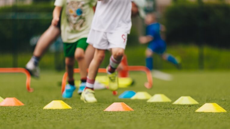 Kids train on a field with colorful cones during practice, showing balance between sports and school