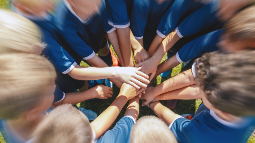 A youth team forms a group huddle with hands stacked together outdoors