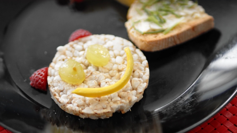 A plate with a rice cake smiley face made from fruit, showing a fun snack for active kids