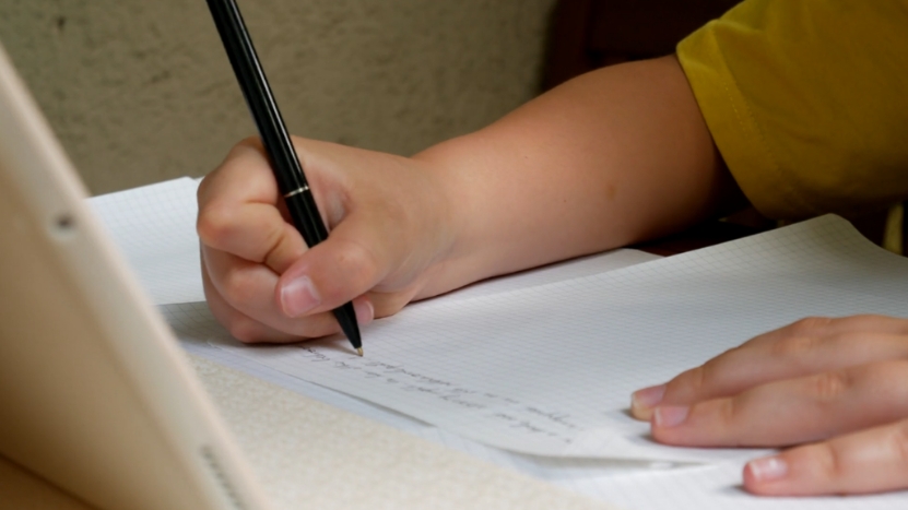A student writes notes in a notebook with a black pen at a desk