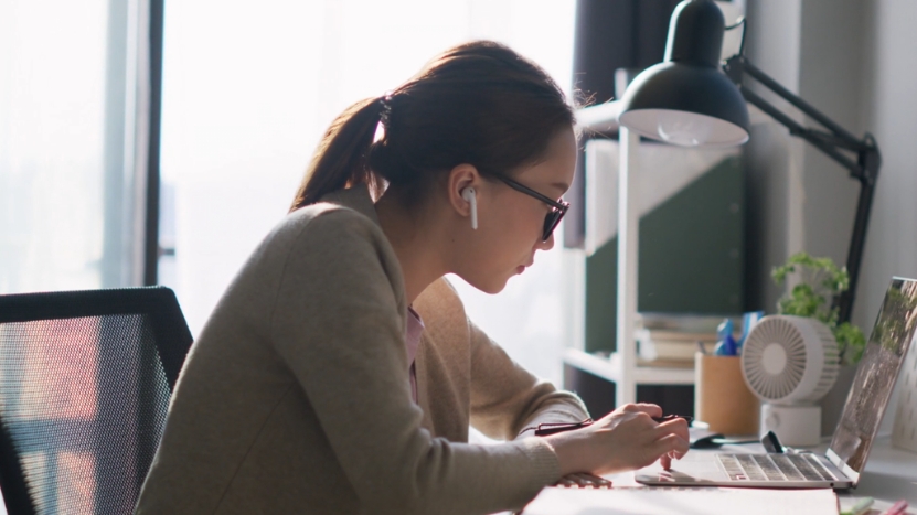 Woman studies at her desk with a laptop and earphones in a bright home workspace