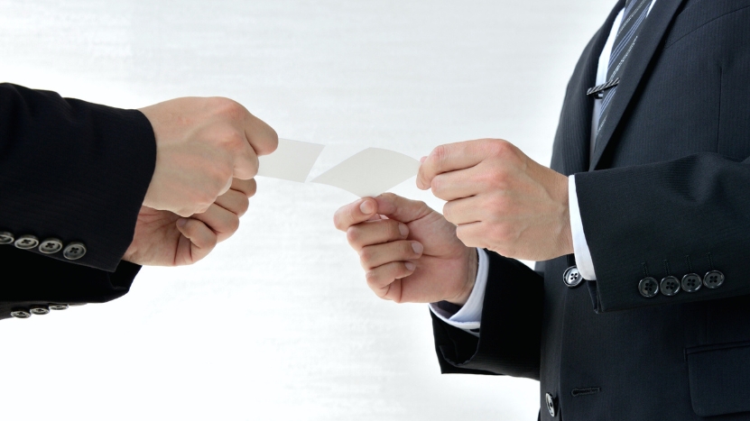 Two professionals in suits exchange business cards during a formal meeting